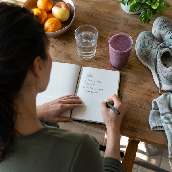 A person practicing healthy habits with a journal, water, smoothie and walking shoes